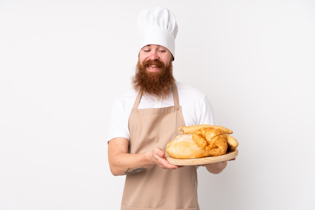 Redhead man in chef uniform. Male baker holding a table with several breads with happy expression