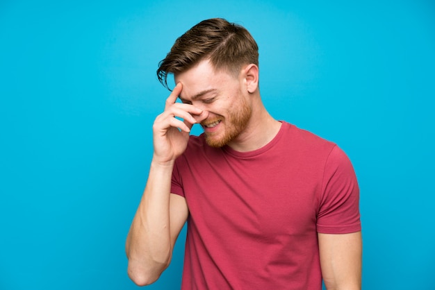 Redhead man on isolated blue wall laughing