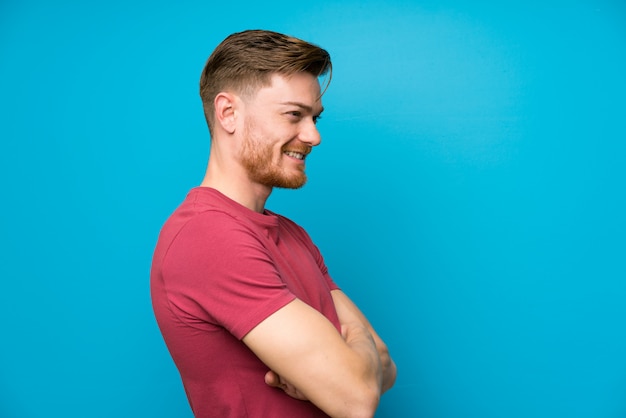 Redhead man on isolated blue wall standing and looking to the side