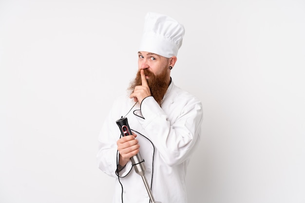 Redhead man using hand blender over isolated white doing silence gesture
