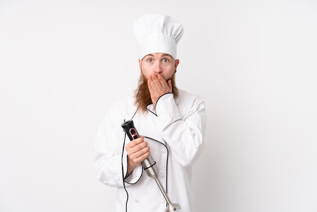 Redhead man using hand blender over isolated white wall with surprise facial expression