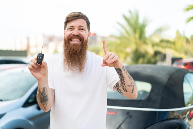 Redhead man with beard holding car keys at outdoors pointing up a great idea