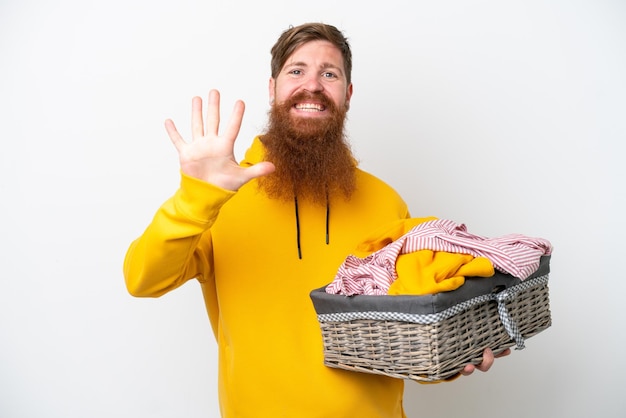 Redhead man with beard holding a clothes basket isolated on white background counting five with fingers