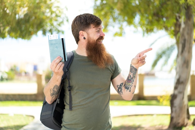 Redhead man with beard holding a passport at outdoors pointing to the side to present a product