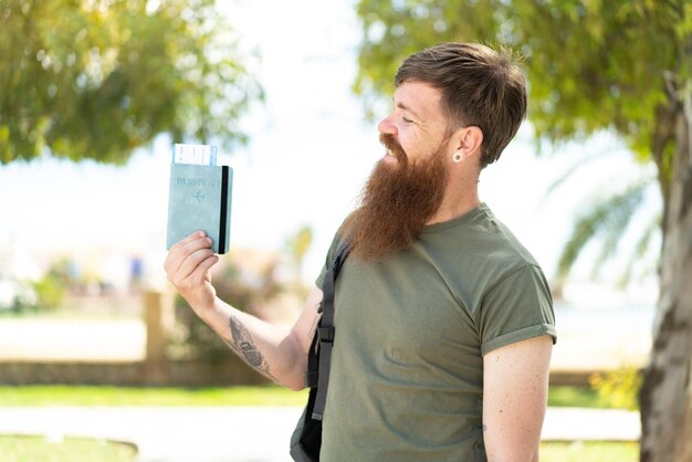 Redhead man with beard holding a passport at outdoors with happy expression