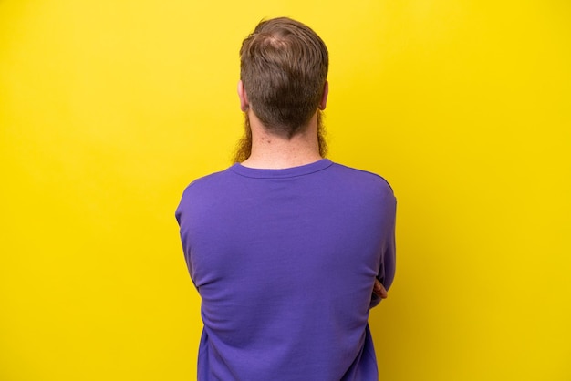 Redhead man with beard isolated on yellow background in back position