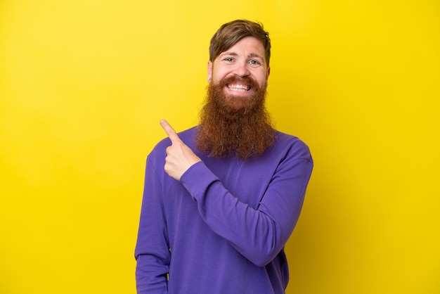 redhead man with beard isolated on yellow background pointing to the side to present a product