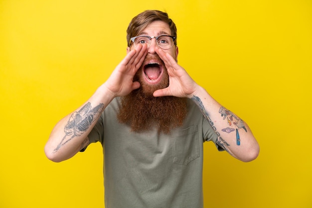 Redhead man with beard isolated on yellow background shouting and announcing something