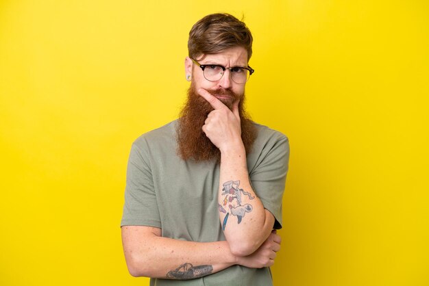 Redhead man with beard isolated on yellow background thinking
