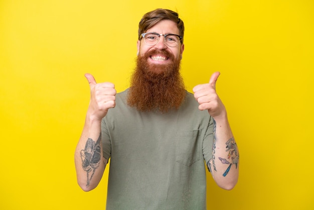 Redhead man with beard isolated on yellow background with thumbs up gesture and smiling