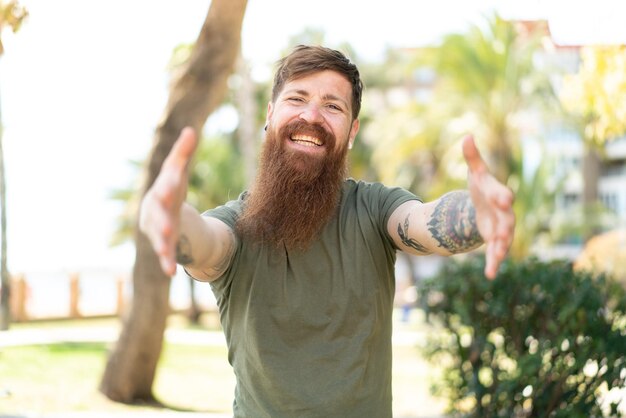 Redhead man with beard presenting and inviting to come with hand