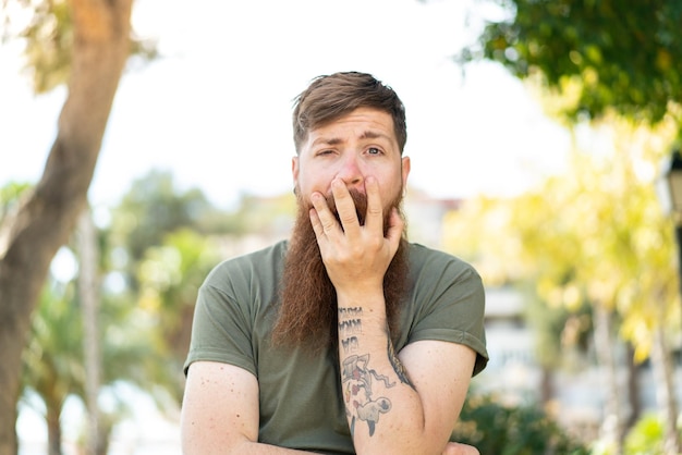 Redhead man with beard surprised and shocked while looking right