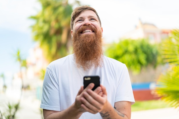 Redhead man with beard using mobile phone and looking up