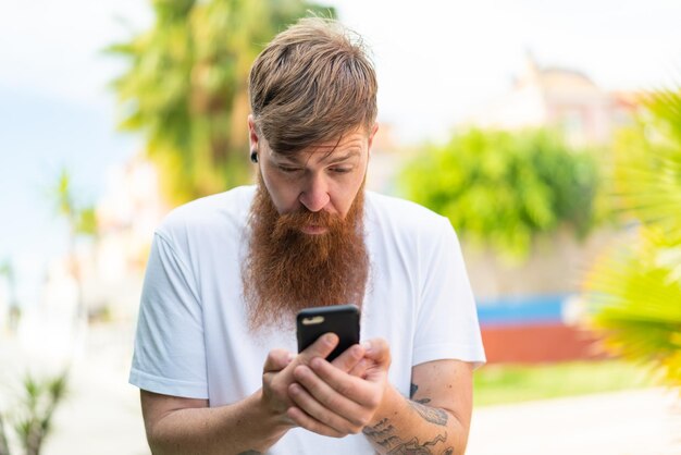Рыжий мужчина с бородой с помощью мобильного телефона