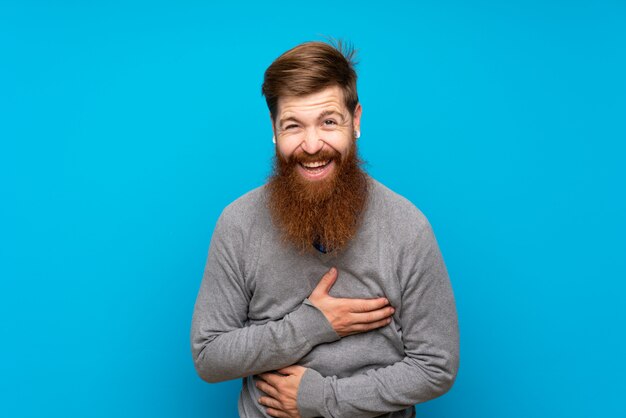 Redhead man with long beard over blue wall smiling a lot