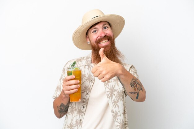 Redhead man with long beard drinking a cocktail on a beach isolated on white background giving a thumbs up gesture