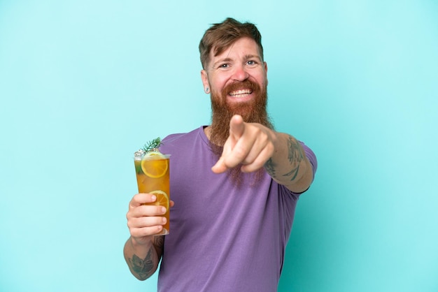 Redhead man with long beard holding a cocktail isolated on blue background points finger at you with a confident expression