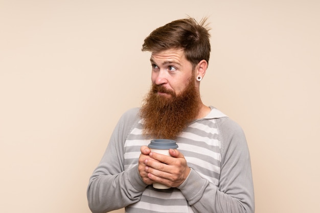 Redhead man with long beard holding coffee to take away