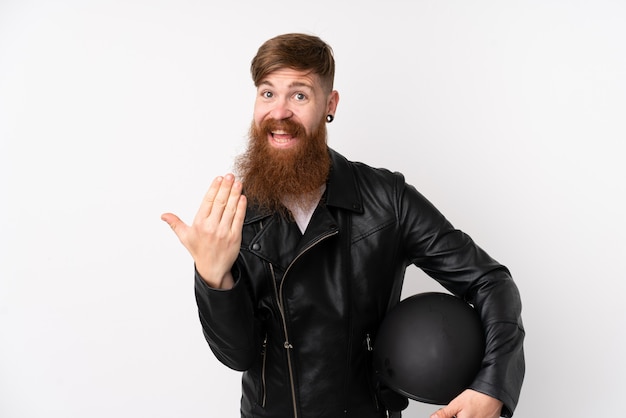 Redhead man with long beard holding a motorcycle helmet over isolated white wall inviting to come