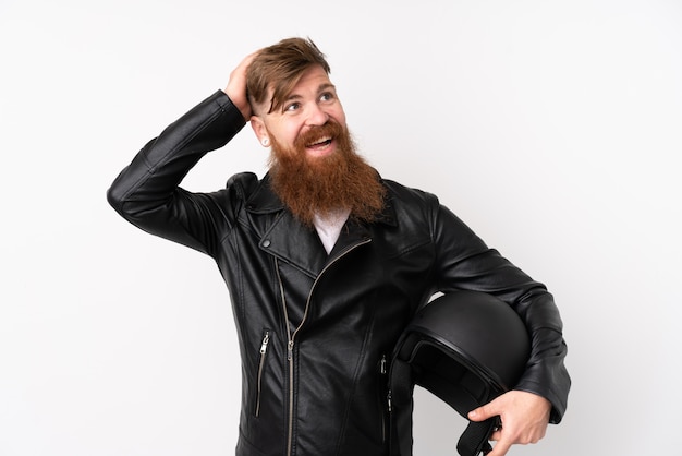 Redhead man with long beard holding a motorcycle helmet over isolated white wall laughing