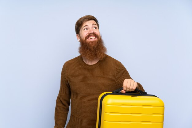 Redhead man with long beard holding a suitcase looking up while smiling