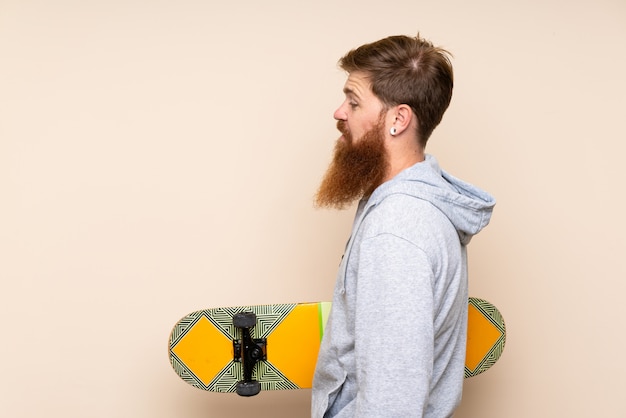 Redhead man with long beard over isolated background with skate in back position