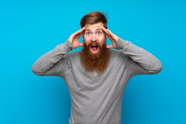 Redhead man with long beard over isolated blue with surprise expression