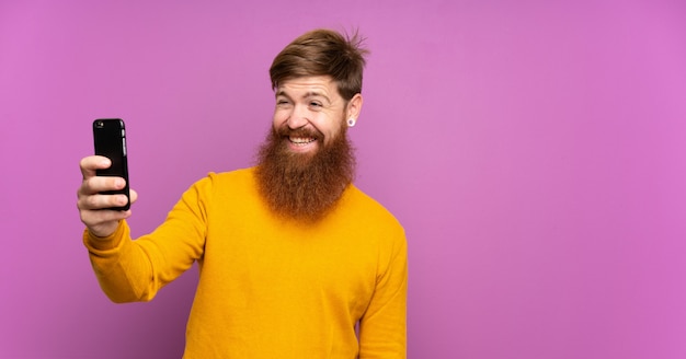 Рыжий мужчина с длинной бородой на изолированных фиолетовый делает селфи