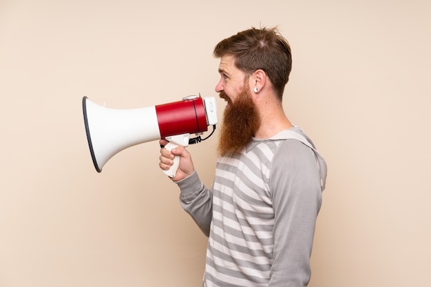 Рыжий мужчина с длинной бородой над изолированной стеной, кричащий через мегафон