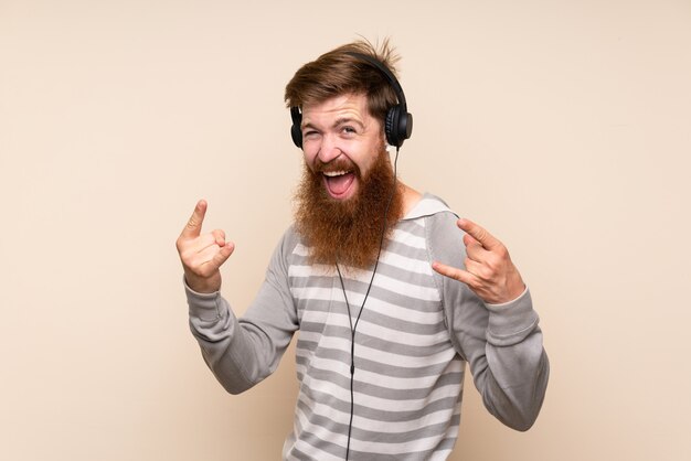ヘッドフォンで携帯電話を使用して踊る孤立した壁の上の長いひげを持つ赤毛の男