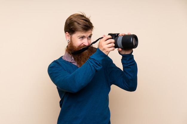 Redhead man with long beard over isolated wall with a professional camera