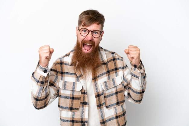 Redhead man with long beard isolated on white background celebrating a victory in winner position