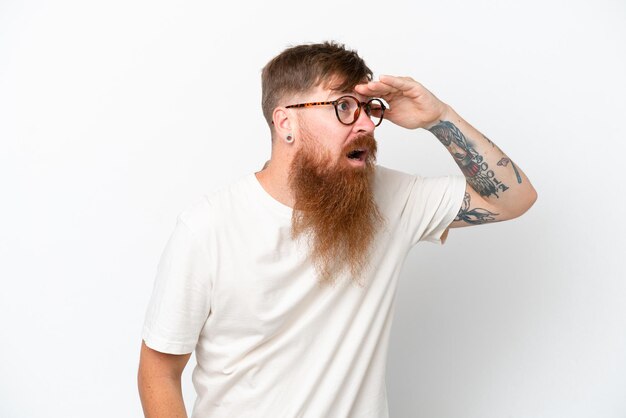 Redhead man with long beard isolated on white background looking far away with hand to look something