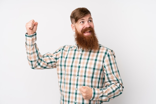 Redhead man with long beard over isolated white wall celebrating a victory