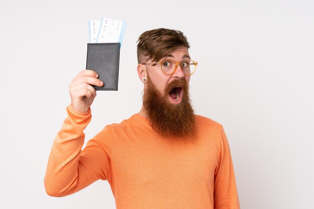 Рыжий мужчина с длинной бородой на изолированной белой стене счастлив в отпуске с паспортом и билетами на самолет