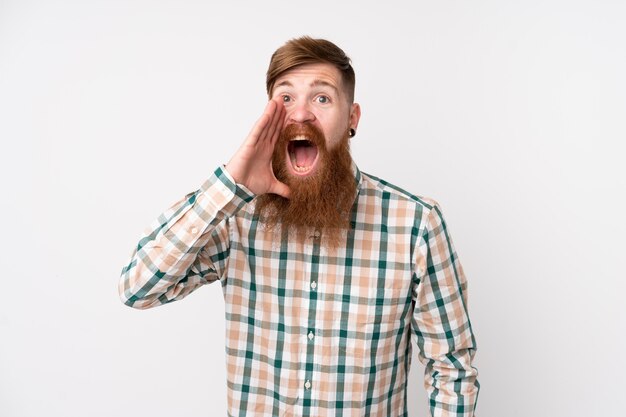 Redhead man with long beard over isolated white wall shouting with mouth wide open