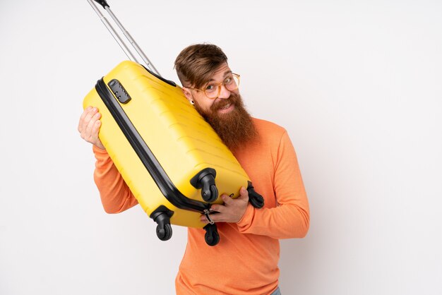 Redhead man with long beard over isolated white wall in vacation with travel suitcase