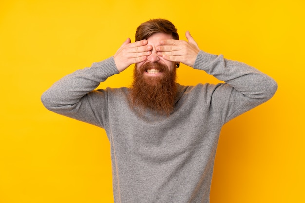 Рыжий мужчина с длинной бородой на изолированной желтой стене, закрыв глаза руками