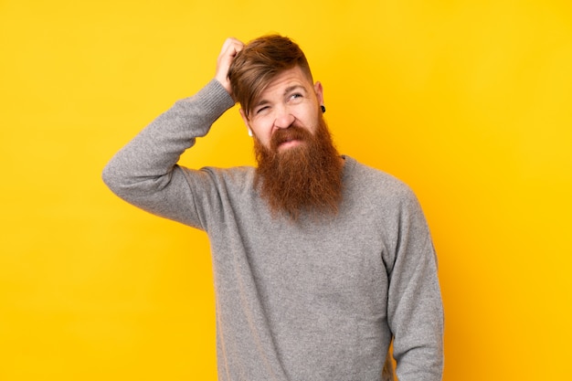 Redhead man with long beard over isolated yellow wall having doubts while scratching head