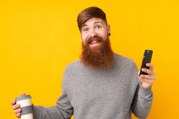 Рыжий мужчина с длинной бородой на изолированной желтой стене ведет разговор с кем-то по мобильному телефону