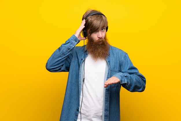 Uomo di redhead con barba lunga sul muro giallo isolato ascoltando musica con le cuffie