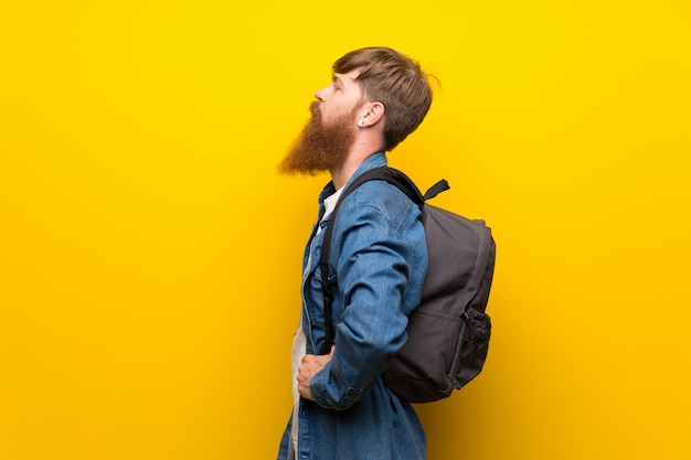 Redhead man with long beard over isolated yellow wall with backpack