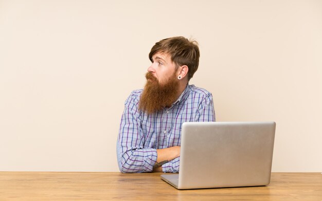 Redhead man with long beard in a table with a laptop looking side