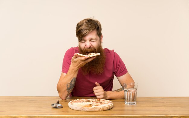 Рыжий мужчина с длинной бородой в столе и с пиццей