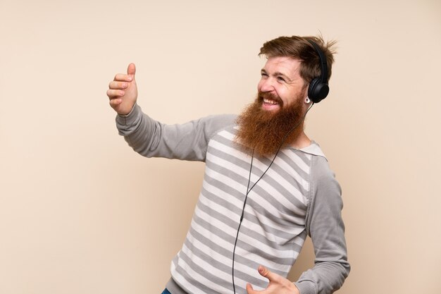 Redhead man with long beard using the mobile with headphones and dancing