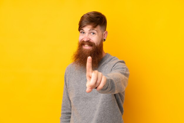 Redhead man with long beard over yellow wall showing and lifting a finger