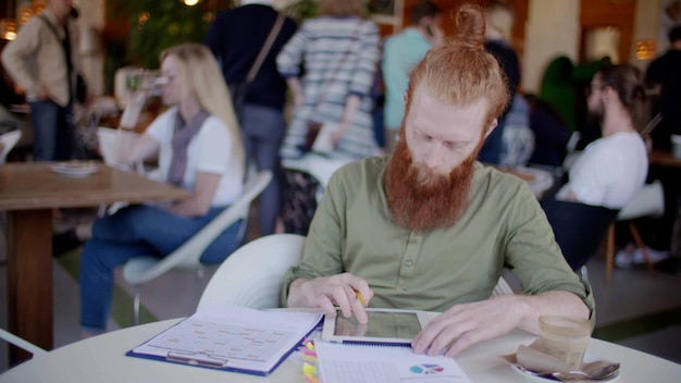 Redhead man working in cafe using digital tablet