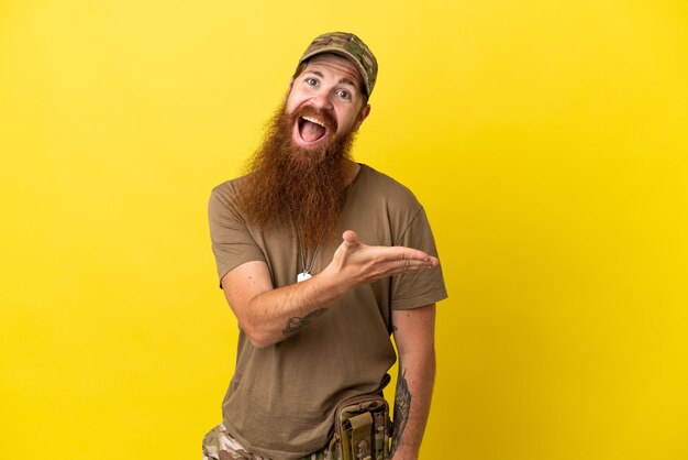 Photo redhead military man with dog tag isolated on yellow background presenting an idea while looking smiling towards