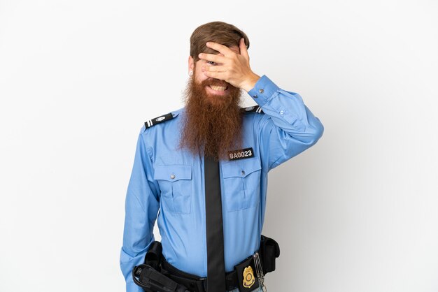 Redhead police man isolated on white background covering eyes by hands and smiling