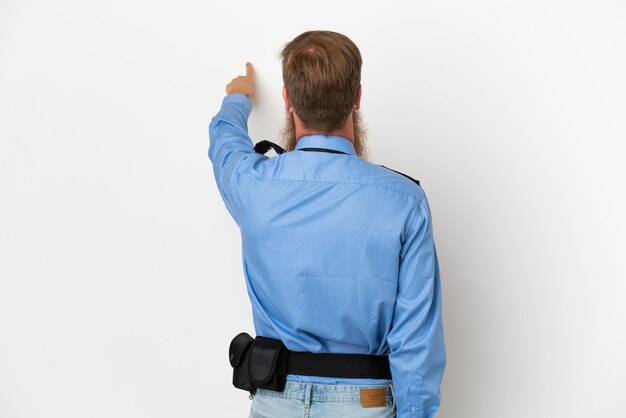 Redhead police man isolated on white background pointing back with the index finger